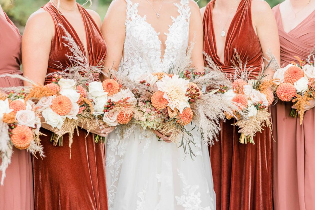 Bridesmaids wearing orange dresses holding bouquets of oranges and ivory flowers. 
